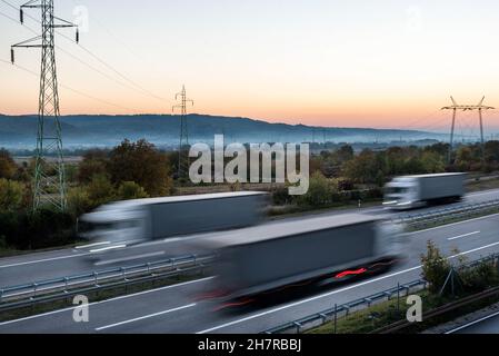 Camions et voitures de livraison en conduite à grande vitesse sur une route à travers le paysage rural. Mouvement flou rapide sur l'autoroute. Scène de fret sur le mois Banque D'Images