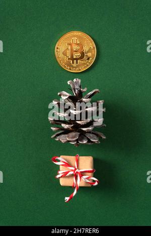 Sapin de Noël concept fait de cônes de pin, cadeau et pièce de monnaie en bitcoin sur fond vert.Photo verticale. Banque D'Images