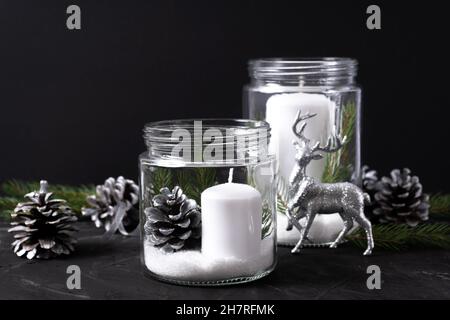 Bougies blanches dans des pots en verre avec des cônes de pin et des branches d'épinette sur fond noir.Le concept de chandeliers à l'intérieur pour noël Banque D'Images