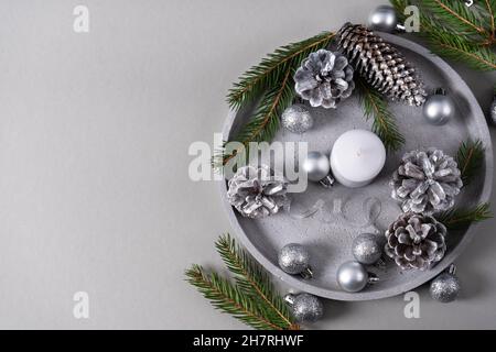 Plateau en béton avec une bougie, des cônes de pin, des branches de sapin, des boules de Noël argentées sur fond gris avec espace de copie.Vue de dessus Banque D'Images