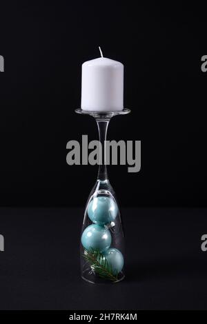 Bougie blanche sur la tige d'un verre de champagne avec boules de Noël bleues sur fond noir.Le concept d'un chandelier à l'intérieur pour la ne Banque D'Images