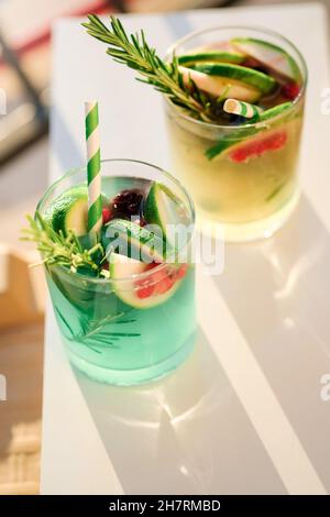 Mojito, cocktail vert alcoolisé frais ou limonade à la chaux, aux baies rouges, à la glace et au romarin dans des verres..concept de vocation d'été.vue du dessus.Soleil et ombres. Banque D'Images