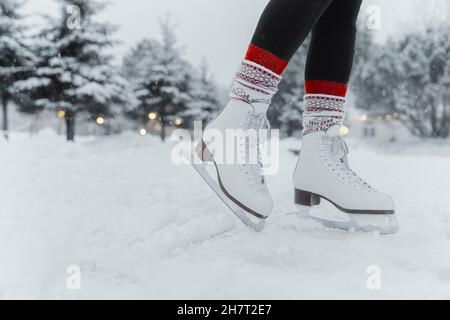 Patinage artistique femme patinant sur la glace à la patinoire extérieure pendant la chute de neige portant des bottes en cuir blanc femelle.Activités de plein air en famille sports d'hiver Banque D'Images