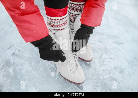 Patineuse de glace nouant des lacets de figure skates chaussures pour aller skate à la patinoire.Sports d'hiver.Gros plan des mains et des pieds. Banque D'Images