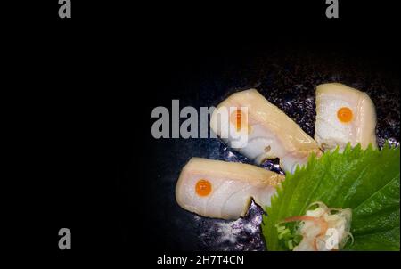 Poisson blanc Aburi coupé en tranches sur le dessus avec des œufs de saumon servis sur une assiette en céramique bleu foncé. Profitez de l'expérience Omakase au restaurant japonais Sushi. Banque D'Images