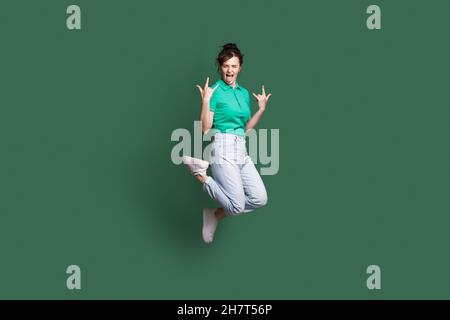 Photo pleine grandeur d'une jeune folle femme de race blanche qui saute en montrant la langue.Panneau Rock'n'roll.Isolé sur fond vert Banque D'Images