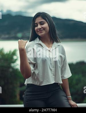 Jeune femme colombienne attrayante portant une chemise blanche et un pantalon noir posant à l'extérieur Banque D'Images