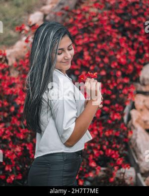 Jeune femme colombienne attrayante portant une chemise blanche et un pantalon noir posant près des fleurs Banque D'Images