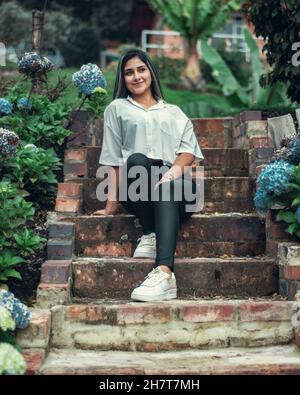 Jeune femme colombienne attrayante portant une chemise blanche et un pantalon noir posé sur les escaliers Banque D'Images