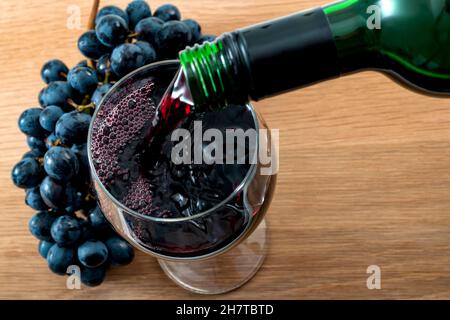 Boisson alcoolisée, fabrication du vin et de l'industrie de l'alcool concept avec vin rouge versé d'une bouteille dans un verre sur une table en bois dans le cadre rustique de Banque D'Images