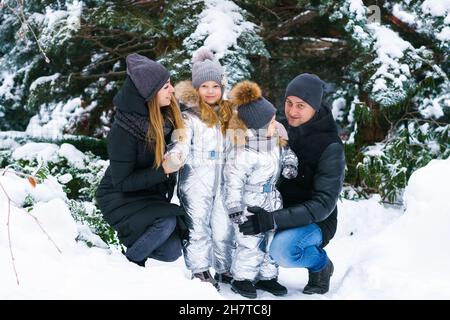 Maman avec papa et fils et fille en hiver dans la cour près de l'arbre de noël recouvert de neige.Chutes de flocons de neige.Portrait de la belle famille en vêtements d'hiver près de l'arbre de noël.Famille en forêt d'hiver. Banque D'Images