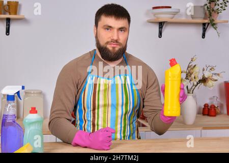 Jeune homme beau barbu dans la cuisine, nettoie à l'aide de détergents, de brosses, de vaporisateurs Banque D'Images