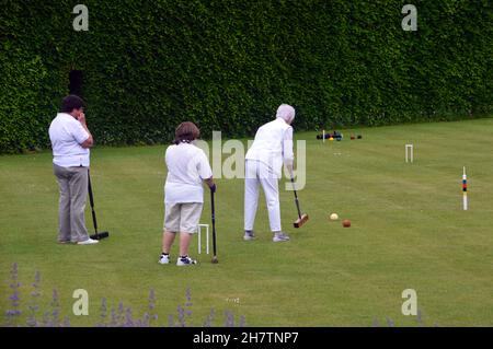 Une femme mûre qui atteint le ballon avec un maillet en bois sur la pelouse du Croquet à Levens Hall & Gardens, parc national de Lake District, Cumbria, Angleterre, Royaume-Uni. Banque D'Images