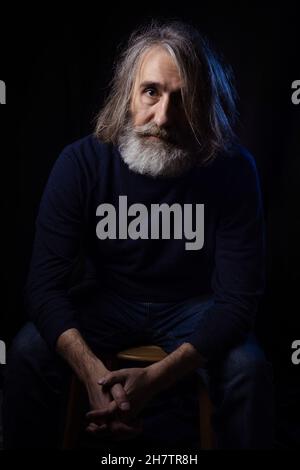 Portrait d'un homme âgé à poil gris barbu en vêtements sombres sur fond sombre.Le concept est le vieillissement, la tristesse, la sagesse. Banque D'Images