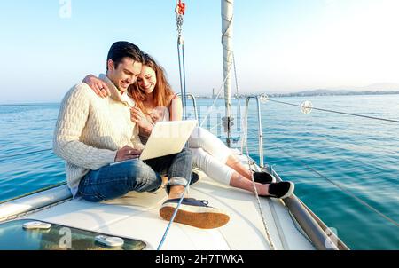 Jeune couple amoureux sur bateau à voile ayant plaisir à travailler à distance à l'ordinateur portable - heureux luxe style de vie sur yacht voilier - concept de technologie avec influenceur Banque D'Images