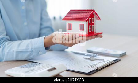 Le concept immobilier le réalteur présentant son travail à son client en mettant le modèle de maison rouge sur ses paumes et en levant ses mains un littl Banque D'Images