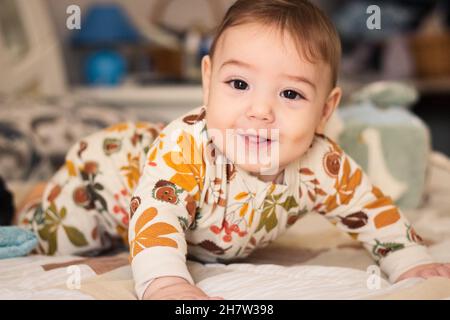 Adorable bébé sur un lit portant une combinaison de barboteuse pyjama combinaison regardant directement l'appareil photo Banque D'Images