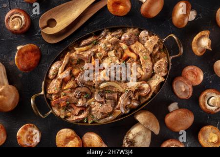 Ragoût de bœuf, de champignons et de viande dans une sauce crémeuse, dans une casserole avec les ingrédients, verser le plat sur un fond sombre Banque D'Images