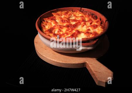 Pâtes Penne dans une assiette rustique sur un plateau en bois isolé sur fond noir. Banque D'Images