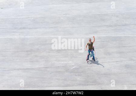 Vue de dessus d'un homme en lunettes de soleil saluant tout en montant sur un vélo rétro Banque D'Images