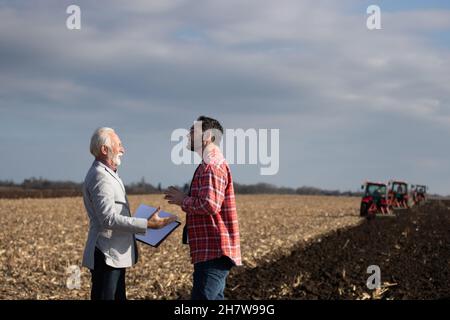 Un homme d'affaires expérimenté s'est présenté à un jeune agriculteur sur le terrain, devant des tracteurs, en automne Banque D'Images