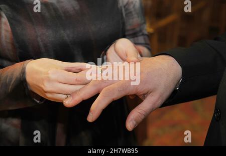 Anneau d'or que la mariée place sur le doigt du marié le jour de son mariage.Vue rapprochée des mains. Banque D'Images