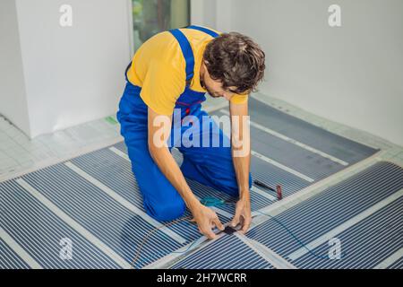 Master installe le film sur sol chaud dans la pièce.Installation de chauffage au sol Banque D'Images