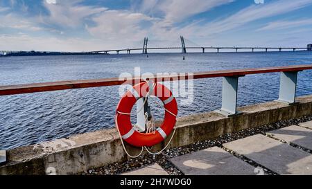 Bouée de sauvetage orange sur la rambarde de la jetée sur fond d'un grand pont et d'un ciel avec des nuages par une journée ensoleillée Banque D'Images