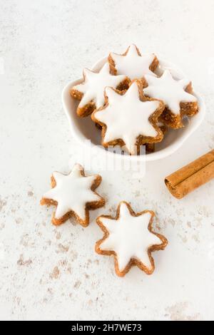 Biscuits aux étoiles de cannelle, Zimtsterne allemand traditionnel dans un bol blanc sur fond à motifs avec bâton de cannelle.Copier l'espace. Banque D'Images