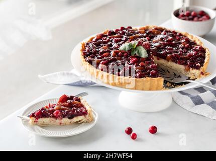 Une tarte au cheesecake aux canneberges avec une tranche sur une assiette, contre une fenêtre ensoleillée. Banque D'Images