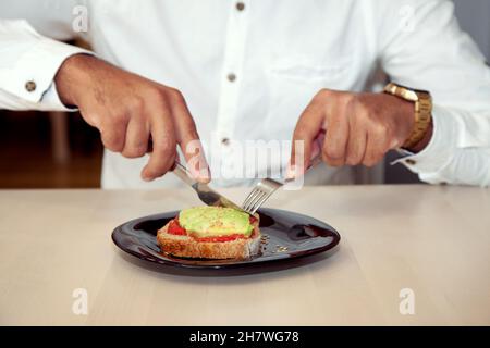 Garçon mangeant.Garçon dans un café.Homme coupant des toasts.Toast à l'avocat et à la tomate.Coupe de garçon.Homme mangeant.Style de vie.Pause.Homme avec café. Banque D'Images