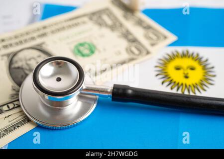 Stéthoscope noir sur fond de drapeau argentin avec billets en dollars américains, concept commercial et financier. Banque D'Images