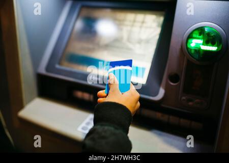 Main d'un jeune homme d'amérique latine avec une carte de crédit bleue sur un caissier de banque, au crépuscule Banque D'Images