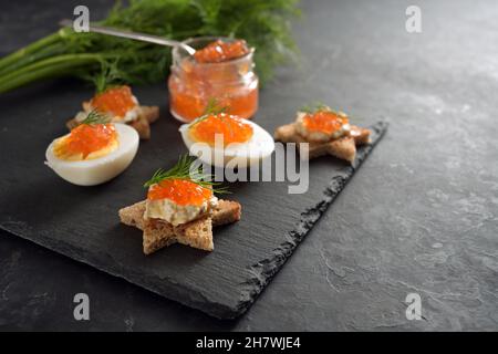 Caviar rouge sur les œufs coupés en deux et sur les canapés grillés en forme d'étoile avec aneth, préparation pour un buffet de Noël festif sur une assiette en ardoise sombre, grand exemplaire Banque D'Images