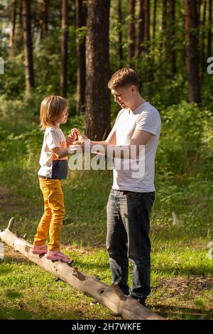 Fille caucasienne de 6 ans marchant sur une bûche tenant la main du père. Père et fille jouant ensemble, rire et s'amuser. Bonne activité en famille Banque D'Images