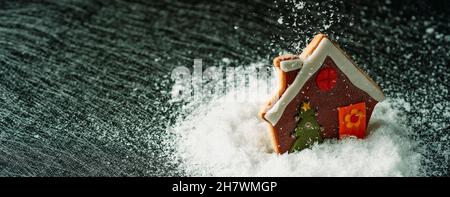 gros plan d'un cookie de noël en forme de maison de pain d'épice sur une pile de fausse neige tout en neige, dans un format panoramique à utiliser comme web b Banque D'Images