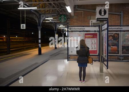 Doncaster, Royaume-Uni, 22 mai 2021: Une femme porte un manteau d'hiver la nuit, tout en lisant les informations sur une plate-forme propre de la gare de doncaster Banque D'Images