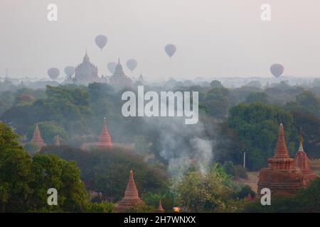 Un petit feu de broussailles brûle sous les ballons d'air chaud, brume matinale au-dessus des temples de Bagan Banque D'Images