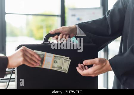 vue rognée d'une femme floue avec des dollars près de l'homme avec mallette, concept anti-corruption Banque D'Images