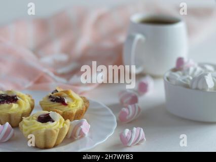 Des gâteaux aux fruits luxuriants avec des amandes sur une soucoupe blanche, des mini guimauves dans une tasse de porcelaine et une tasse de café fort. Banque D'Images