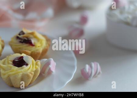 Gâteaux de fruits en éponge avec amandes sur une soucoupe blanche, mini guimauves dans une tasse en porcelaine.Gros plan sur un arrière-plan clair.Mise au point sélective. Banque D'Images