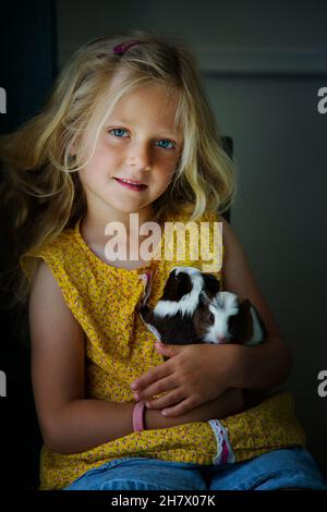 Une petite fille blonde douce de 5 à 6 ans avec son animal de compagnie guinae cochons Banque D'Images