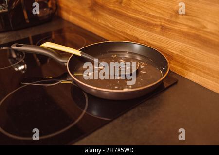 poêle sale avec spatule en plastique après cuisson sur une table de cuisson en verre à induction dans une cuisine moderne Banque D'Images