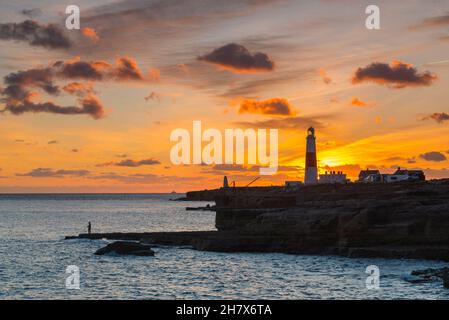 Portland Bill, Dorset, Royaume-Uni.25 novembre 2021.Météo Royaume-Uni.Le ciel au-dessus du phare brille d'orange à Portland Bill à Dorset au coucher du soleil tandis qu'un homme pêche des rochers à la fin d'une journée froide et claire.Crédit photo : Graham Hunt/Alamy Live News Banque D'Images