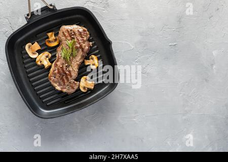 Steak de bœuf grillé aux champignons et aux épices sur une poêle sur fond gris Banque D'Images