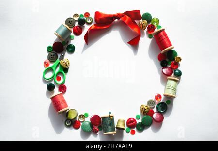 Couronne de Noël en boutons, fils, épingles, ciseaux, rouge à coudre,vert et or sur fond blanc avec ombre.Copier l'espace. Banque D'Images