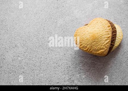 Trois petits gâteaux doux en forme de cœur : vanille, citron, chocolat sur la gauche. Arrière-plan gris, espace de copie. Banque D'Images