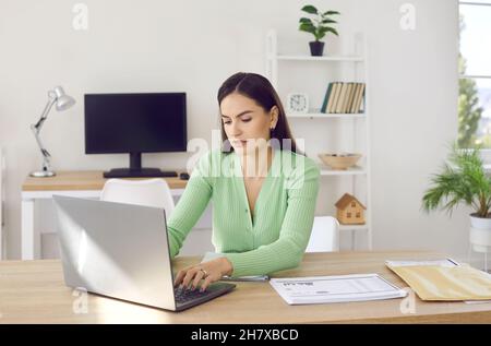 Portrait d'une jeune femme travaillant avec un ordinateur portable et des documents dans un bureau à espace ouvert. Banque D'Images