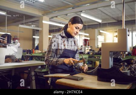 Un ouvrier poinçonné des trous dans le cuir des futures bottes dans l'atelier de l'usine de chaussures Banque D'Images