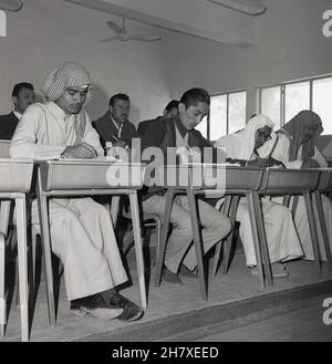 Années 1960, étudiants en ingénierie, hommes, certains portant la robe arabe traditionnelle longueur cheville, un théobe et des coiffures, assis à des bureaux dans une salle de classe, Jeddah, Arabie Saoudite.La découverte de pétrole et d'autres minéraux dans le pays a nécessité un développement de l'éducation et donc une grande poussée a été faite en Arabie Saoudite à ce moment-là pour augmenter l'offre d'éducation dans ce secteur.L'année 1963 a vu la création du Collège du pétrole et des minéraux (CPM) avec un total de 67 jeunes hommes inscrits en septembre 1964.Le collège a ensuite été rebaptisé Université King Fahd de pétrole et minéraux (KFUPM). Banque D'Images